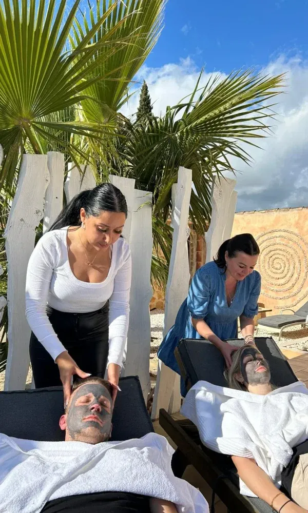 Wellness-Moment im Freien: Zwei Gäste liegen mit Gesichtsmasken unter Palmen, während sie von Wellness-Experten verwöhnt werden.