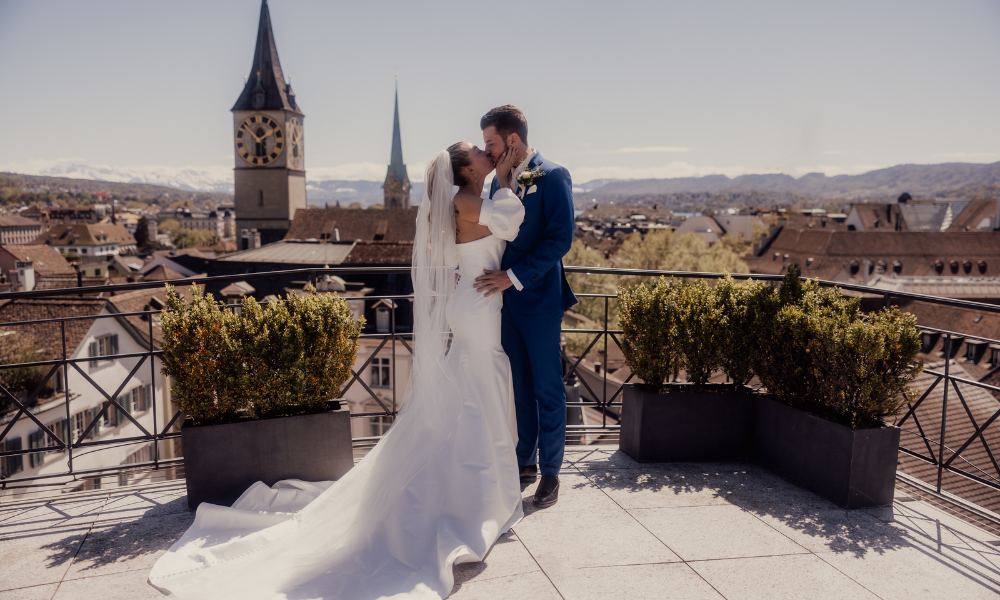 Brautpaar küsst sich über den Dächer von Zürich mit Sonnenschein und blauem Himmel.