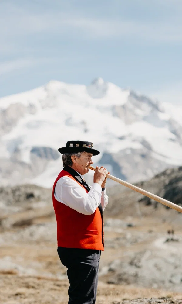 Der Mann mit einem Hut und roter Kleidung. Er spielt ein Instrument in den Bergen.