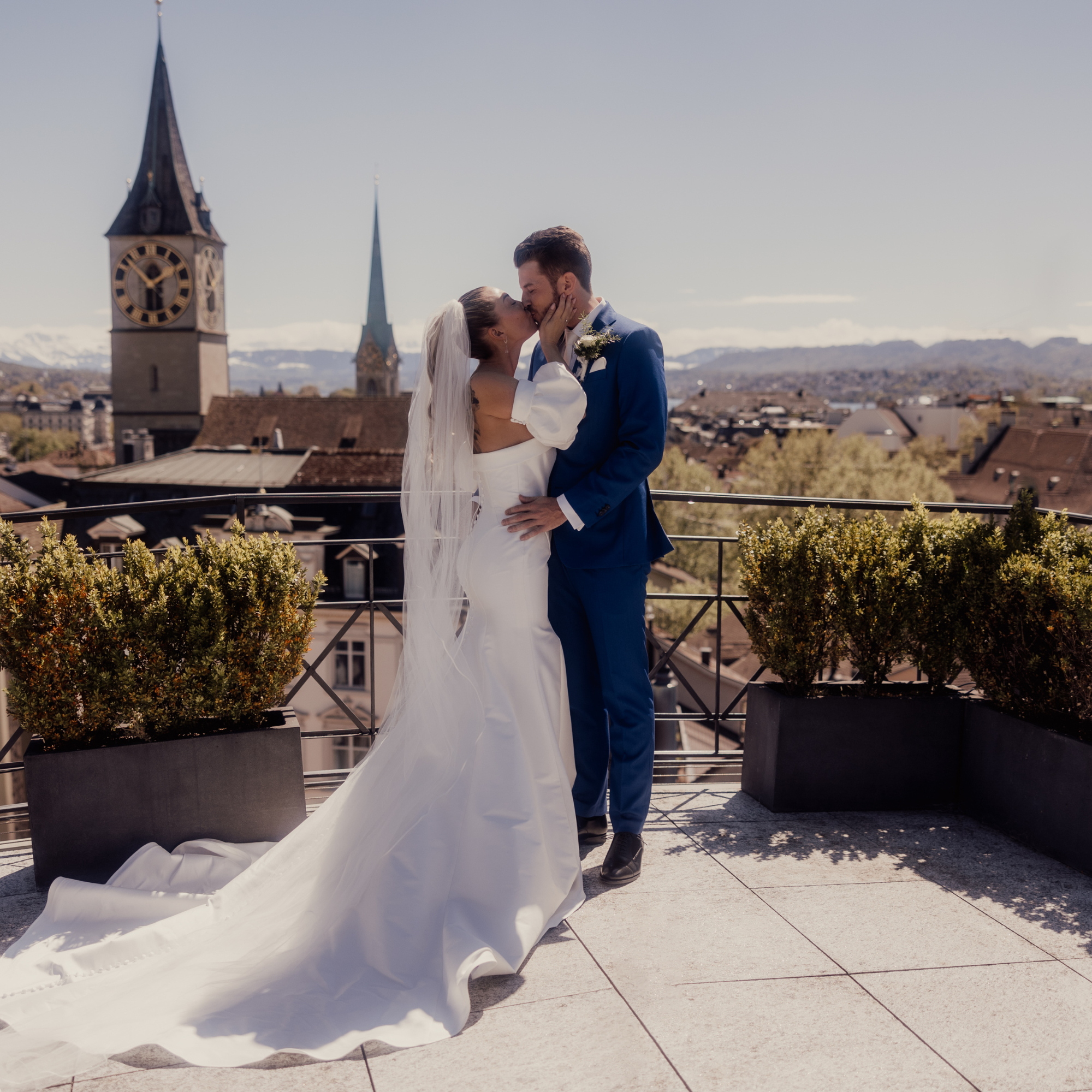Hochzeit in Zürich, mit Aussicht auf Zürich, Brautpaar küsst sich, weisses langes Hochzeitskleid, die Sonne scheint. Das Brautpaar ist verliebt.