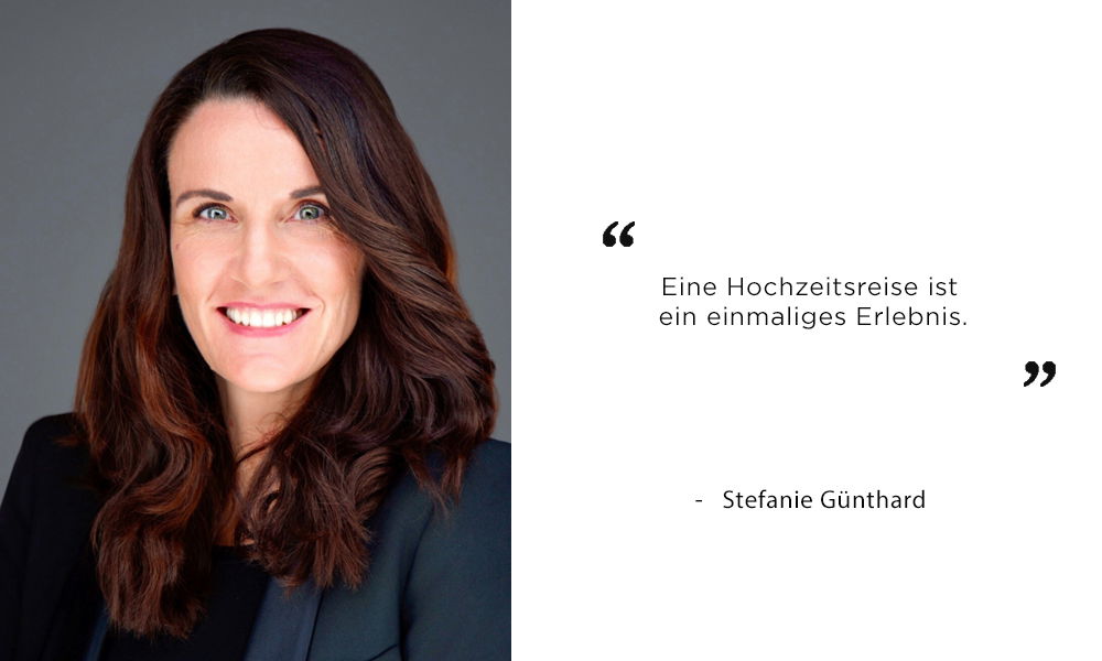 Porträt einer lächelnden Frau mit langen, dunklen Haaren vor einem neutralen Hintergrund. Rechts neben ihr steht ein Zitat: „Eine Hochzeitsreise ist ein einmaliges Erlebnis.“ – Stefanie Günthard. Die Frau trägt ein dunkles Oberteil und repräsentiert eine inspirierende Aussage zum Thema Hochzeitsreisen.