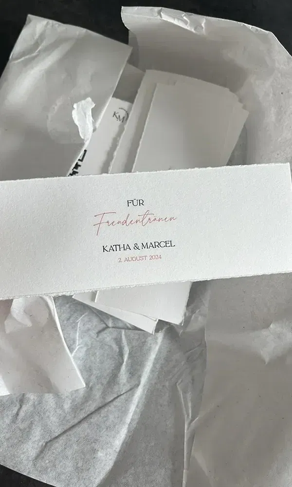 Eine elegante Karte mit der Aufschrift „Für Freudentränen“ und den Namen „Katha & Marcel“ sowie dem Hochzeitsdatum „2. August 2024“, ideal als Hochzeitsdetail.