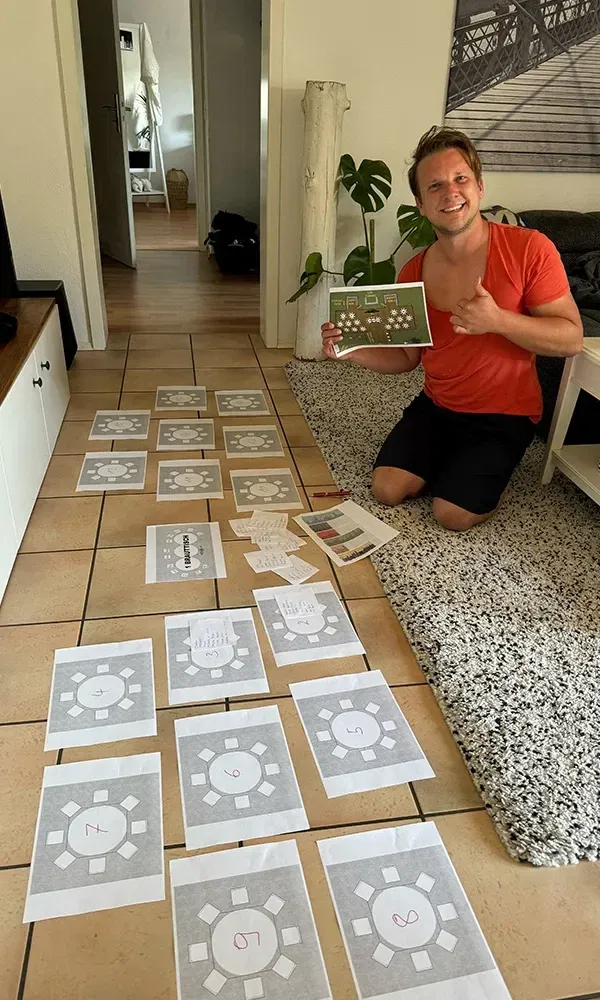 Der Bräutigam sitzt auf dem Boden und ordnet Tischpläne für die Hochzeit an. Die ausgedruckten Pläne und Notizen geben einen Einblick in die detaillierte Vorbereitung des großen Tages.