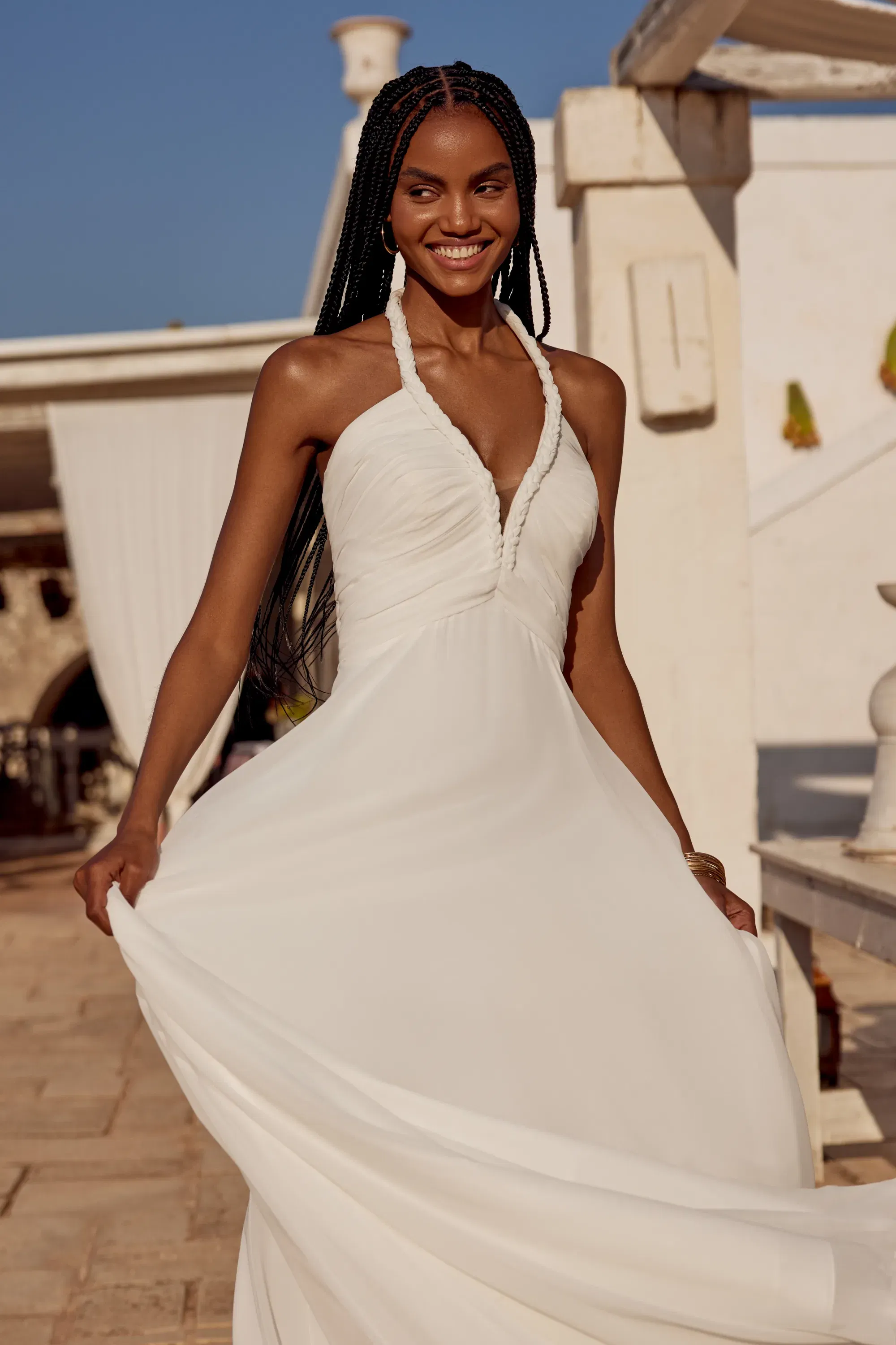 Fließendes Brautkleid mit Neckholder aus weich fallendem Chiffon, getragen von einem lachenden Model im Sonnenlicht.
