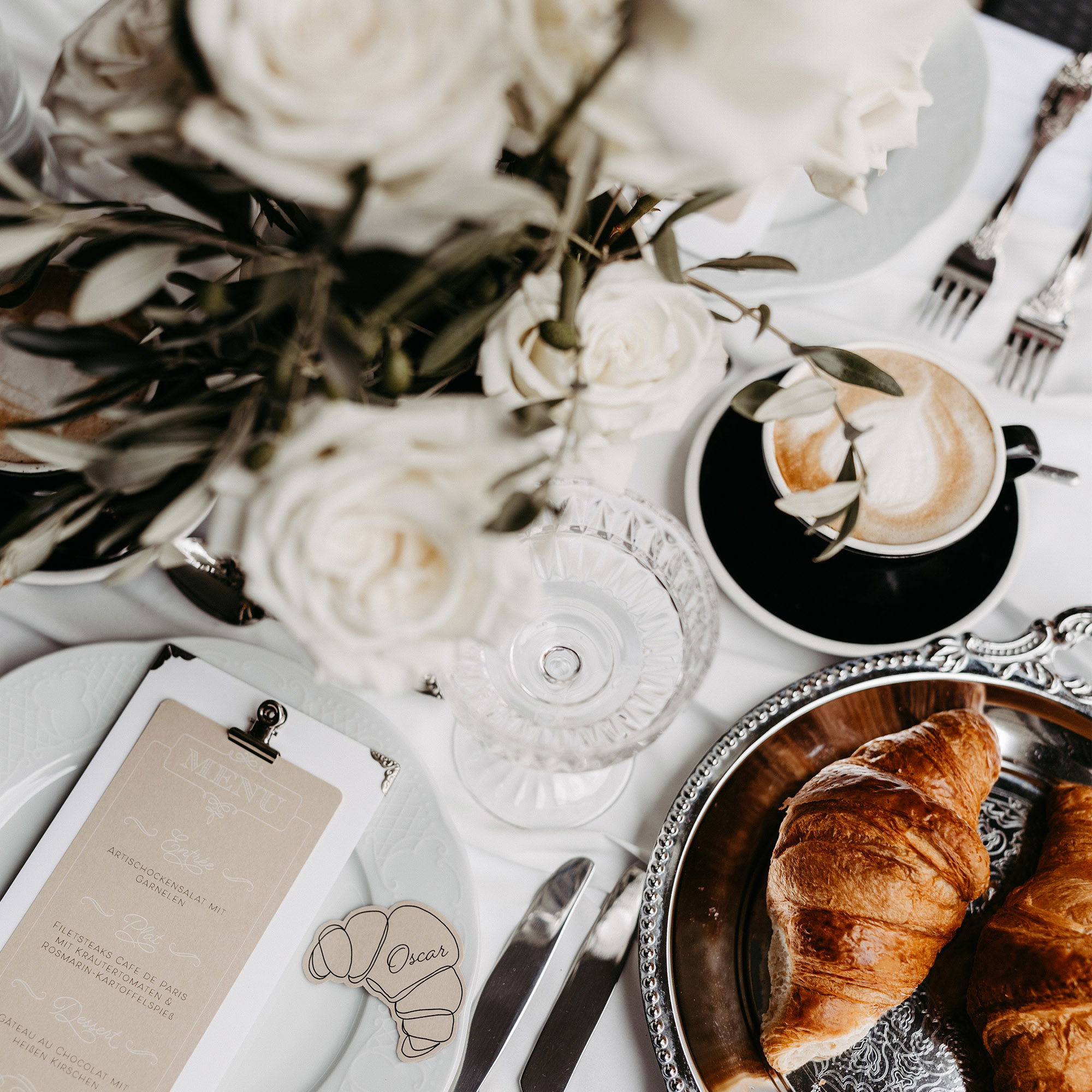Ein gedeckter Tisch mit weißen Blumen, Kaffee und Croissant