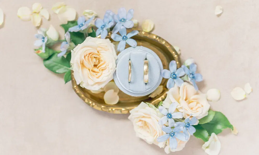 Trauringe drapiert auf einem Goldenen Tablett bestückt mit Blumen.