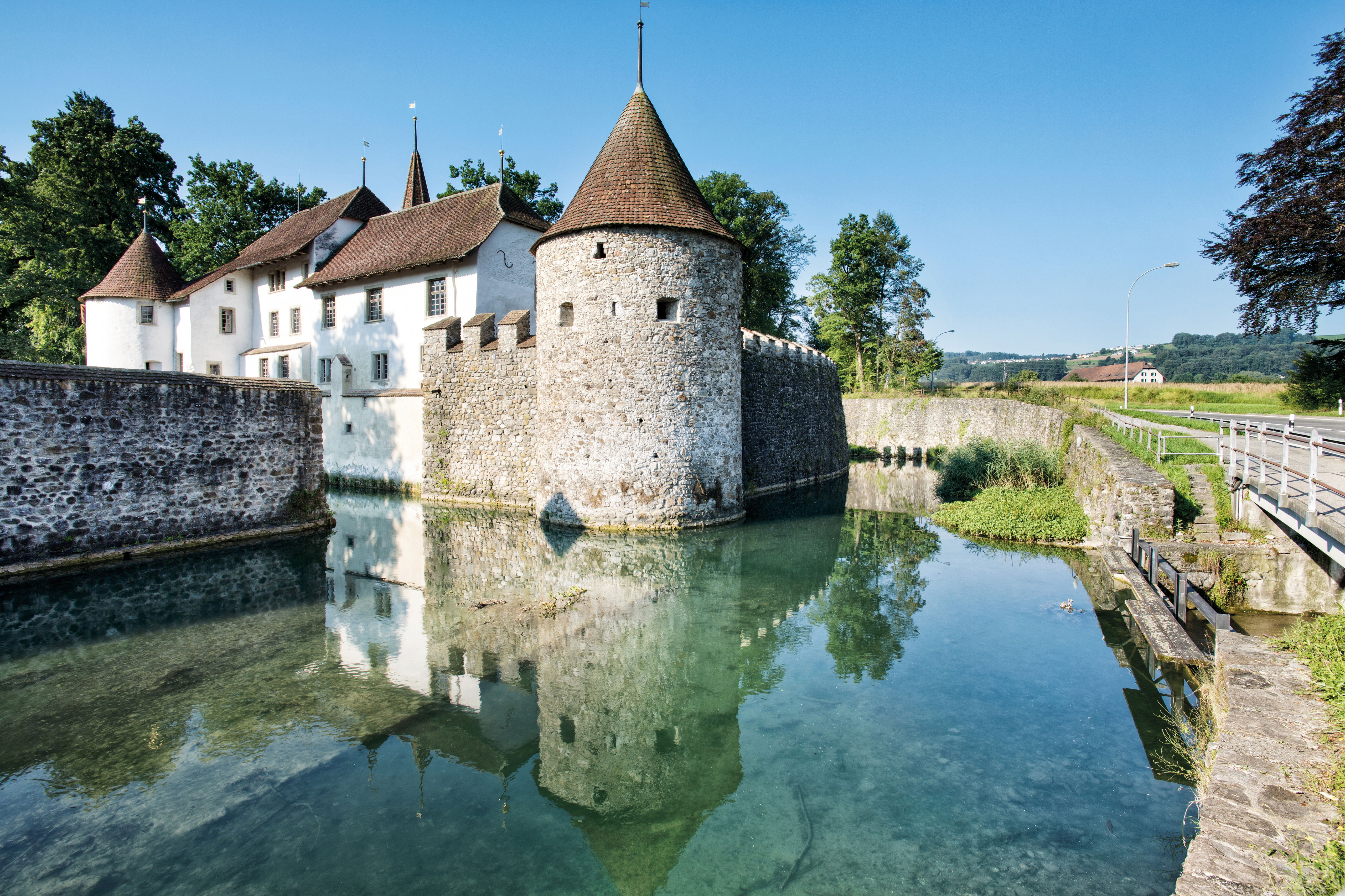 Schloss Hallwyl unter blauem Himmel am Wasser.