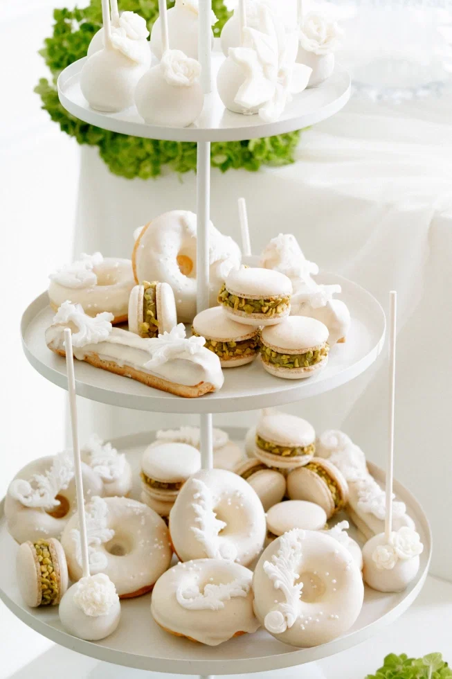 Elegante Hochzeits-Sweettable mit weiß glasierten Donuts, Pistazien-Macarons, Cake Pops und feinem Gebäck auf einer dreistöckigen Etagere.