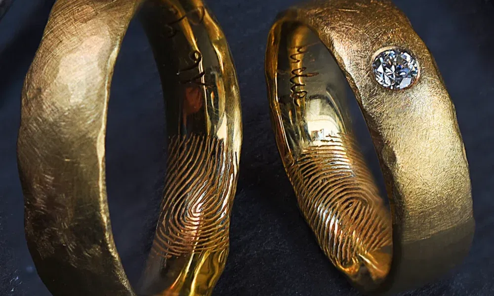 Einzigartige goldene Trauringe, bei denen auf den Innenseiten der Ringe Fingerabdrücke eingraviert sind. Einer der Ringe ist mit einem Diamanten verziert.