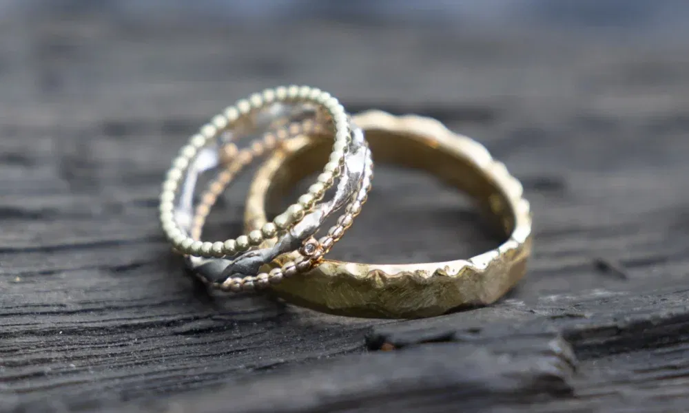 Mehrere filigrane Trauringe in Gold- und Silberfarben, übereinandergestapelt auf einer Holzoberfläche, kombiniert aus verschiedenen Materialien und Designs.