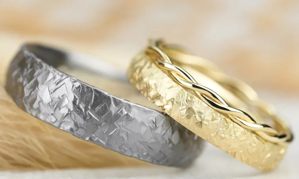 Zwei handgefertigte Trauringe, einer aus Tantal mit gehämmerter Oberfläche, der andere in Gold mit einem geflochtenen Akzent.
