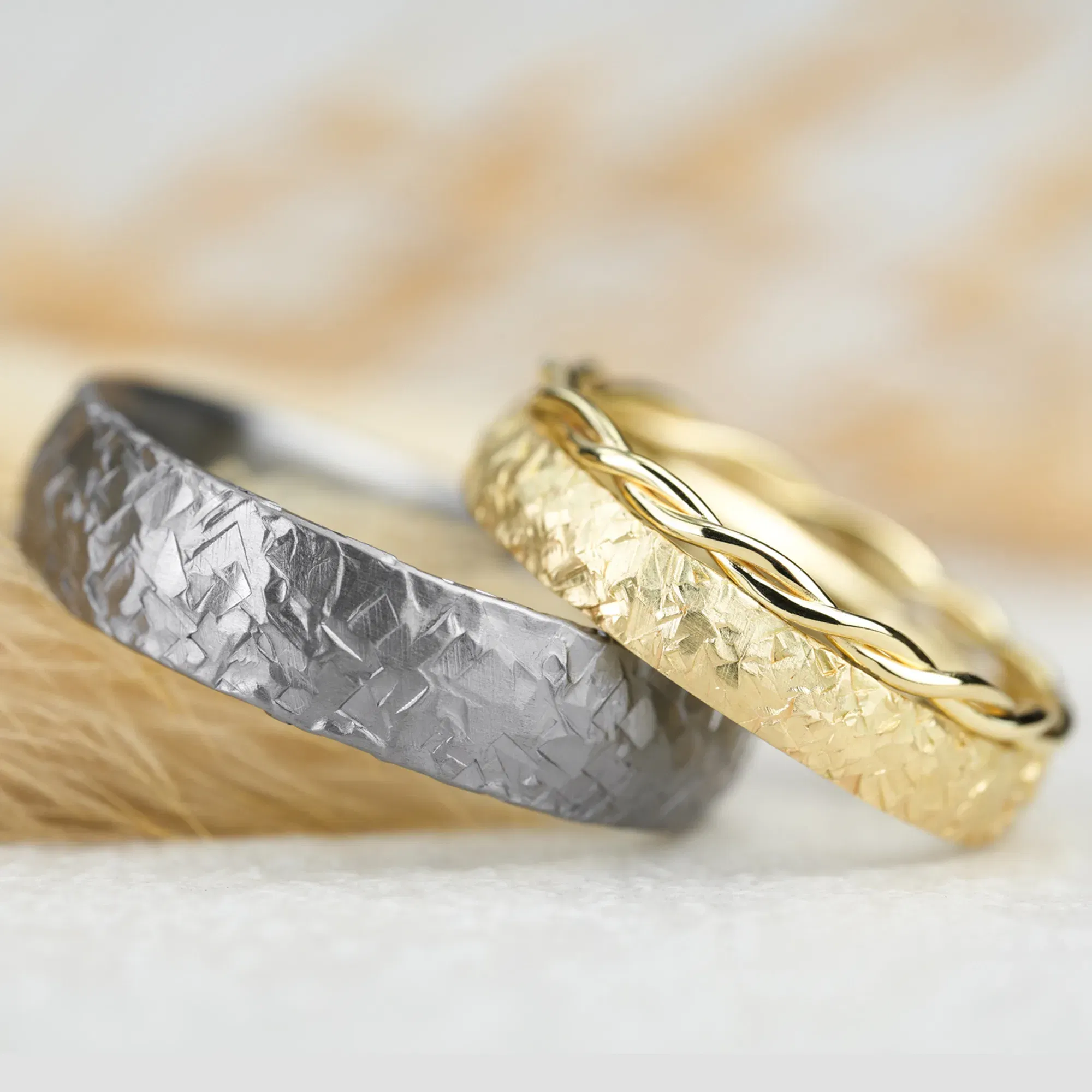 Zwei handgefertigte Trauringe, einer aus Tantal mit gehämmerter Oberfläche, der andere in Gold mit einem geflochtenen Akzent.