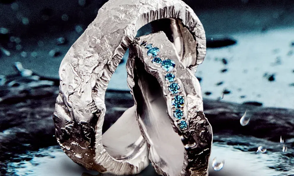 Zwei handgefertigte, rustikale Silberringe mit unregelmäßiger Oberfläche, einer davon mit blauen Edelsteinen besetzt, auf einer Wasseroberfläche fotografiert.