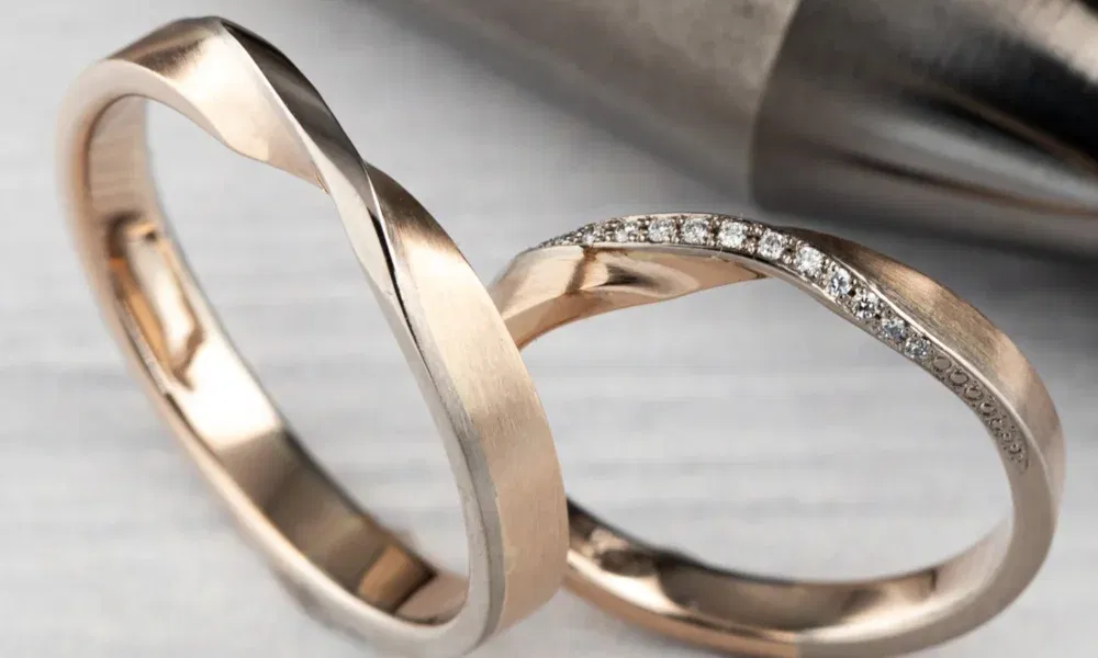 Elegante, minimalistische Eheringe aus Roségold, einer davon mit kleinen Diamanten besetzt, mit einer sanften, geschwungenen Form.