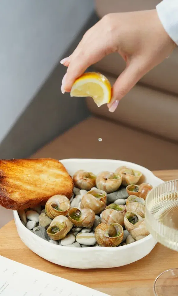 Gourmetgericht mit Escargots und geröstetem Brot, während frischer Zitronensaft über die Schnecken geträufelt wird – ein kulinarischer Moment.