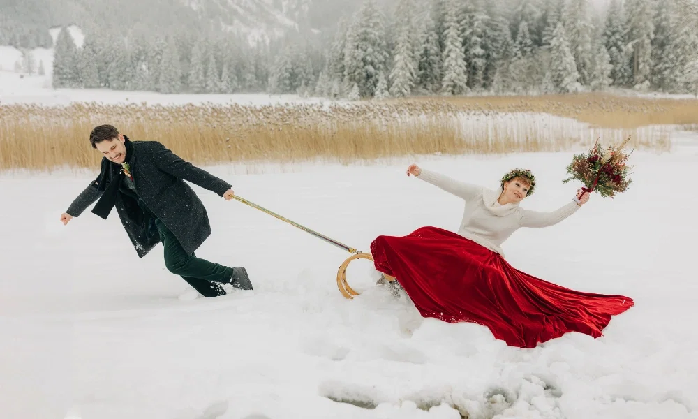 Das Brautpaar im Schnee, die Braut im roten Kleid auf dem Schlitten