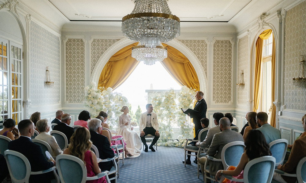 Hochzeit mit Froonck als Trauredner in einem opulenten Raum mit vergoldeten Vorhängen und Blumenschmuck. Das Brautpaar und Gäste erleben eine unvergessliche Zeremonie.