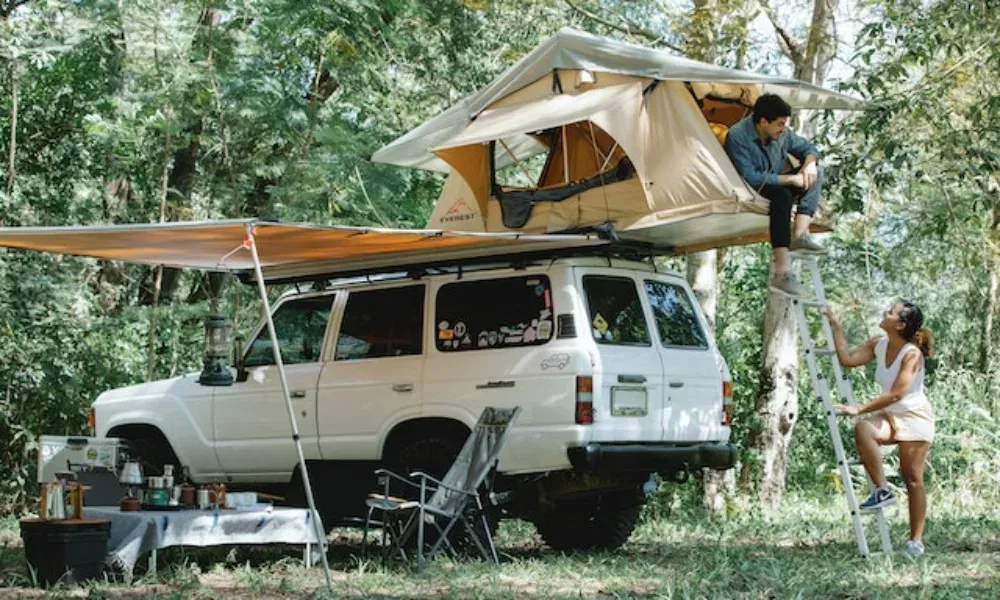 Outdoor-Camping mit einem weißen Jeep, Dachzelt, Sonnensegel und einer gemütlichen Waldküche im Grünen.