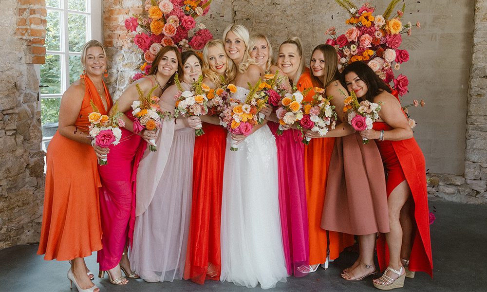 Fröhliche Brautjungfern und die Braut in einer umarmenden Pose mit Blumen.