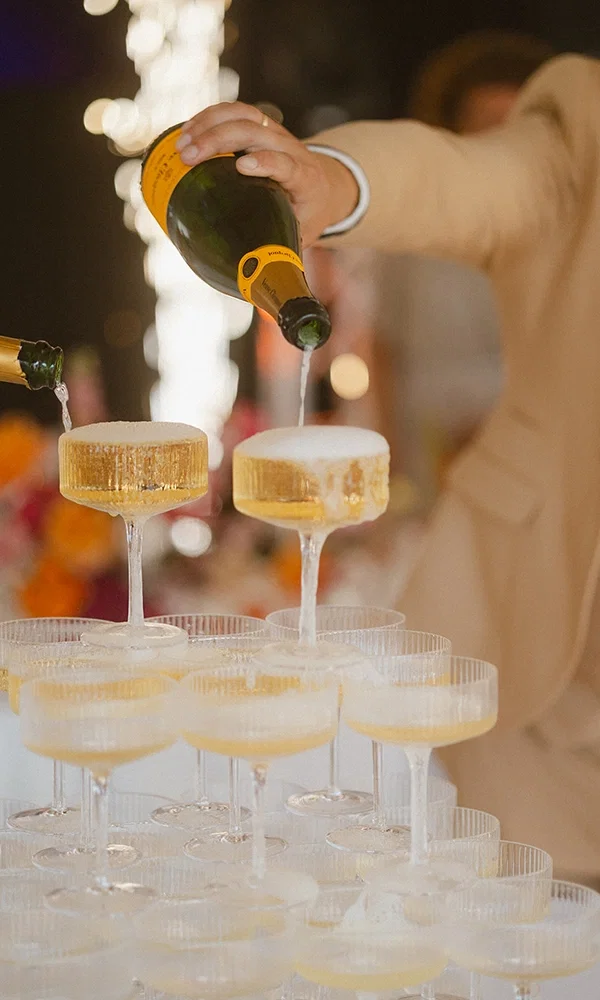Brautpaar füllt einen glitzernden Champagner-Turm bei der Hochzeitsfeier.