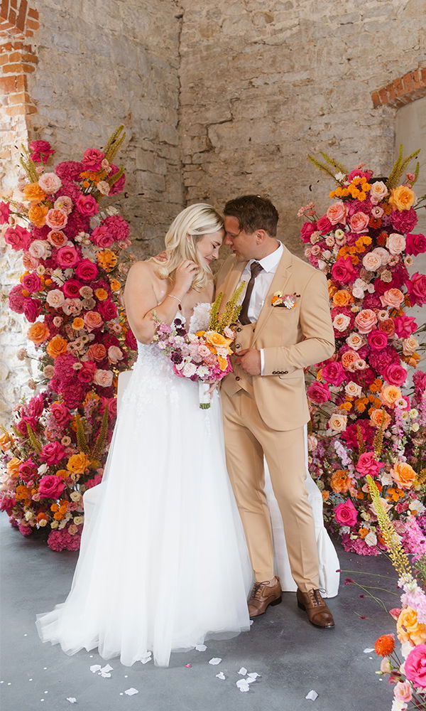 Emotionale Momente zwischen Braut und Bräutigam vor einer blumengeschmückten Wand.