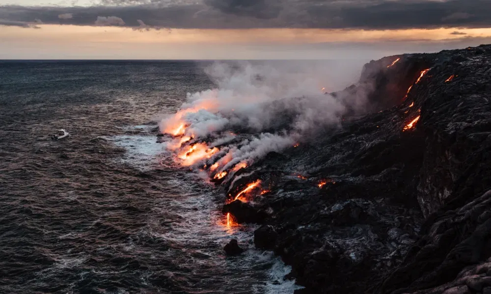 Lava fließt von einer felsigen Küste ins Meer und erzeugt dabei dichte Dampfwolken bei Sonnenuntergang.