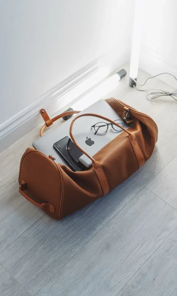 Ein Blick auf den Inhalt einer stylischen Weekender-Tasche: Technik und Essentials für unterwegs, im minimalistischen Interior.