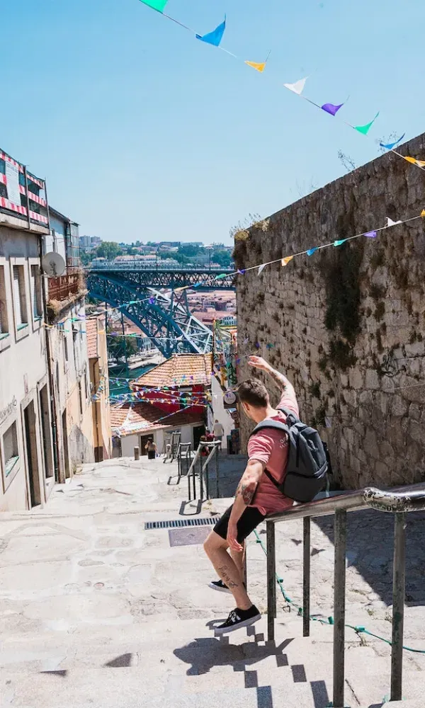 Urbaner Moment in Portugal: Ein Reisender gleitet die Stufen entlang, während sich hinter ihm die Dom-Luís-Brücke und das Stadtpanorama abzeichnen.