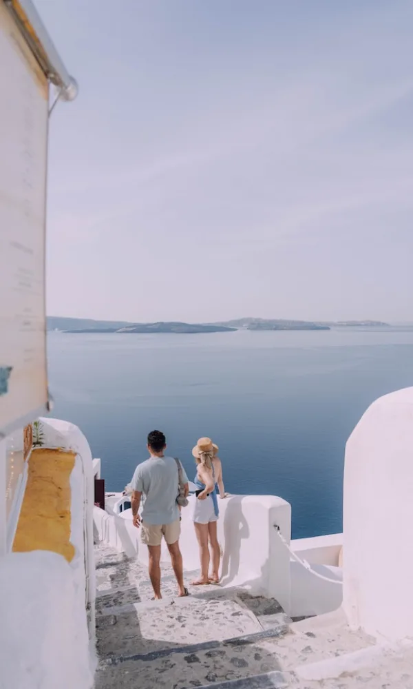 Romantischer Moment auf einer Insel in Griechenland: Ein Paar blickt auf das ruhige Wasser, umgeben von klassisch weißer Architektur.