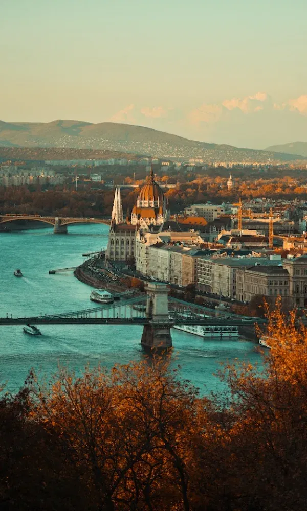 Herbstliche Farben rahmen den Blick auf die Kettenbrücke und das Parlamentsgebäude in Budapest, mit der Donau und Stadtlandschaft im Hintergrund.