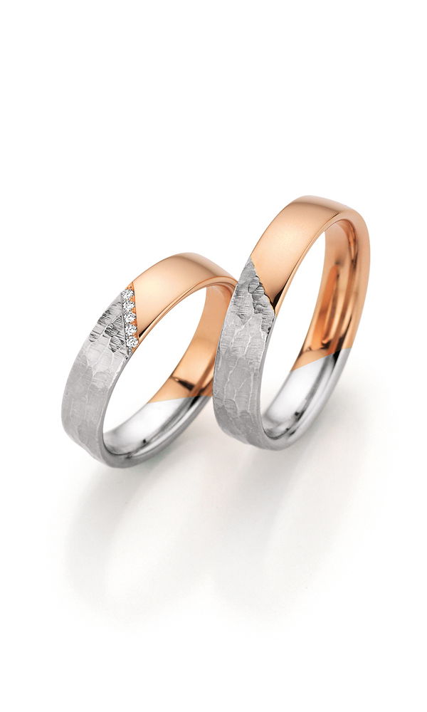 Zweiteilige Eheringe mit einer einzigartigen Mischung aus glänzendem Roségold und markant gehämmertem Weißgold. Der Damenring erhält durch kleine Diamanten entlang der Kante einen zusätzlichen Hauch von Luxus.
