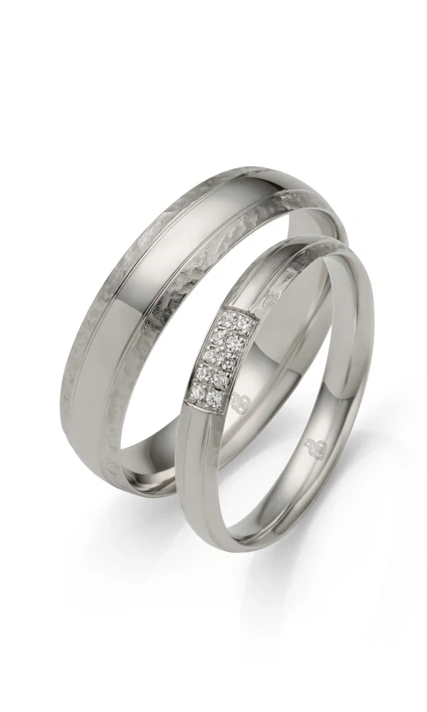 Schlichtes, aber stilvolles Ehering-Duo aus Weißgold. Die Kombination aus gehämmerter Textur und glänzenden Elementen verleiht den Ringen eine besondere Tiefe, während kleine Brillanten den Damenring zieren.