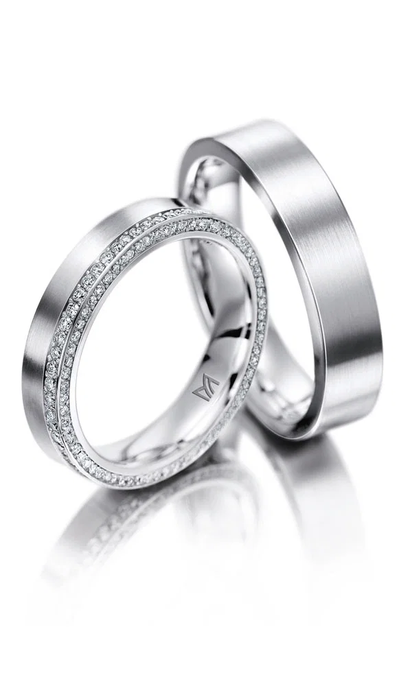 Elegante Partnerringe aus Platin mit seidiger, mattschimmernder Oberfläche. Der Damenring ist mit unzähligen kleinen Brillanten besetzt, die ihm einen luxuriösen Look verleihen, während der Herrenring klassisch gehalten ist.