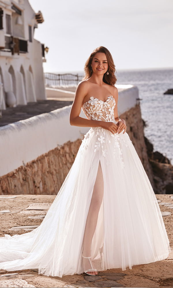 Feminines Brautkleid mit zarten Blumenmustern und Tüllrock, inszeniert in einer malerischen Küstenlandschaft.