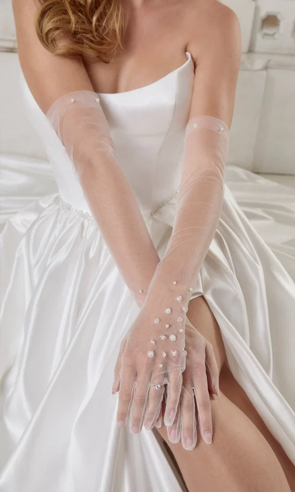 Lange, transparente Tüllhandschuhe mit schimmernden Perlendetails, die für eine stilvolle Ergänzung zum schlichten Brautkleid sorgen. Die dezente Verzierung unterstreicht die Eleganz des Looks.