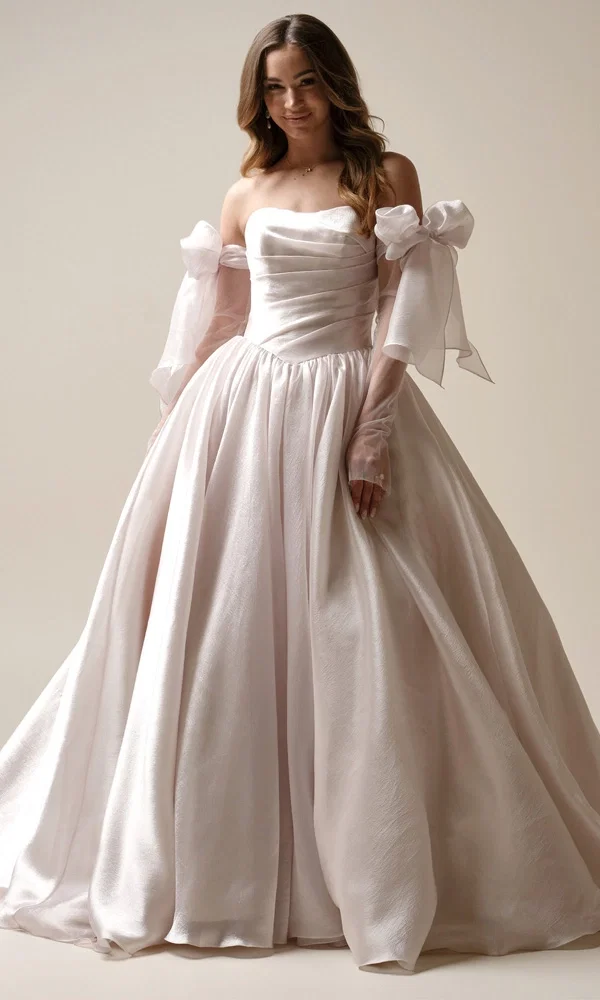 Prinzessinnen-Brautkleid mit Glanzstoff und abnehmbaren Schleifenärmeln – moderner Märchen-Look für den großen Tag.