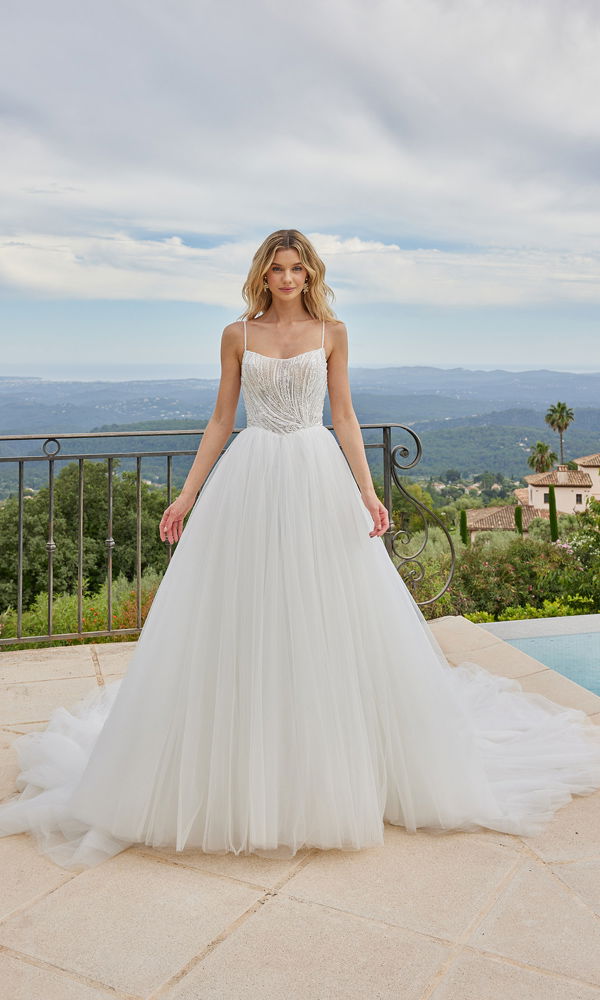 Atemberaubendes Tüll-Brautkleid mit funkelndem Oberteil und leichter Silhouette, aufgenommen vor einem Panorama mit Bergen und Palmen.