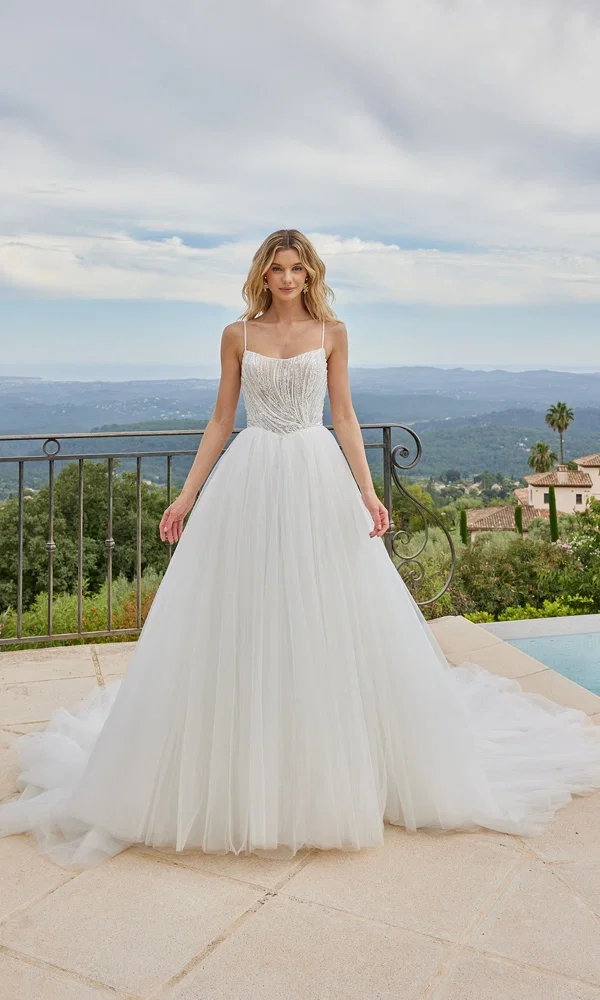 Atemberaubendes Tüll-Brautkleid mit funkelndem Oberteil und leichter Silhouette, aufgenommen vor einem Panorama mit Bergen und Palmen.