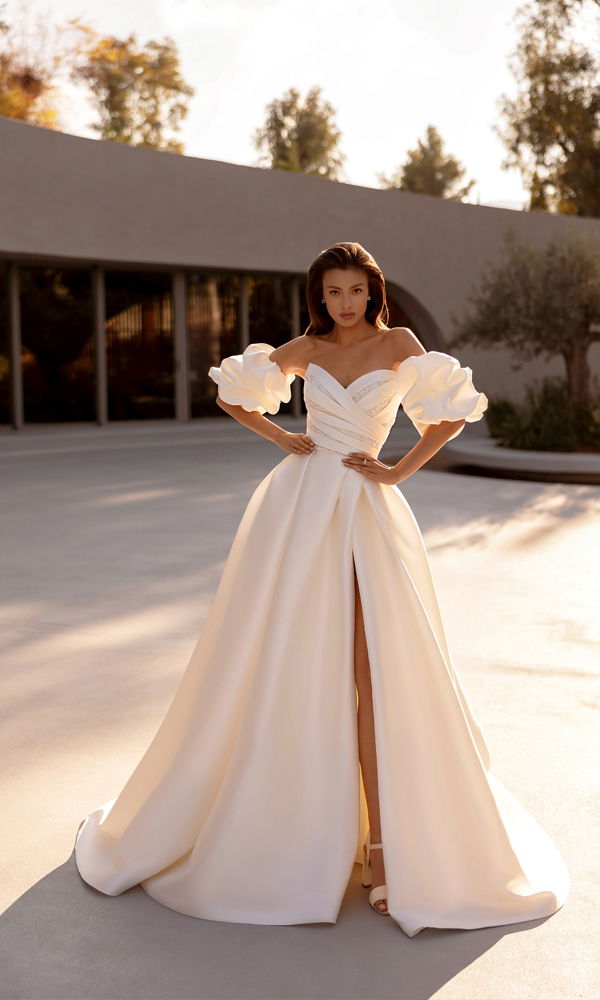 Elegantes Hochzeitskleid mit herzförmigem Ausschnitt und architektonischen Ärmeln – glamouröser Look im Abendlicht.