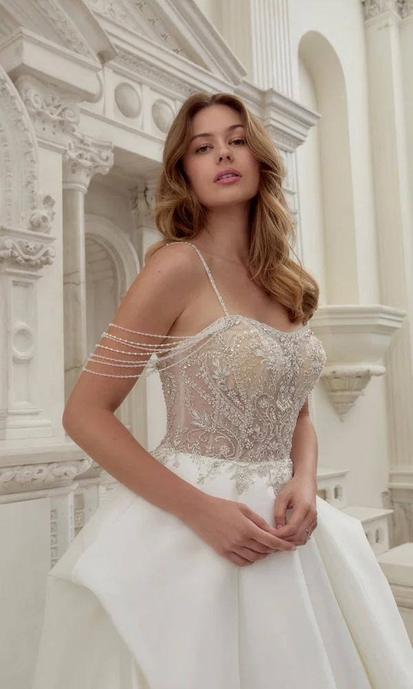 Traumhaftes Kleid mit aufwendigen Stickereien und einer klassischen Silhouette, perfekt inszeniert in einer kunstvollen Architekturkulisse.