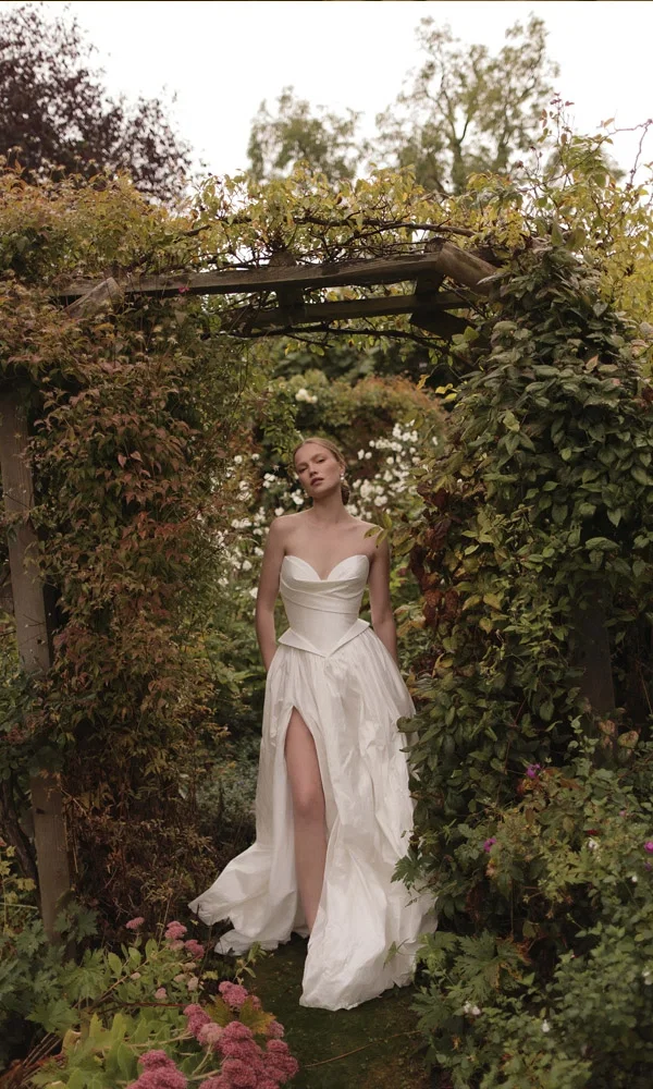 Stilvolles Brautkleid mit asymmetrischem Design, ideal für eine Hochzeit in einem idyllischen Garten voller natürlicher Details.