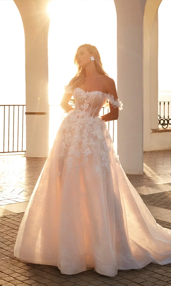 Verspieltes Brautkleid mit Blumenapplikationen und transparenter Corsage – träumerischer Look für eine Hochzeit am Meer.