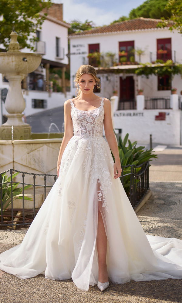 Feminin und modern: A-Linien-Kleid mit aufregendem Schlitz und floralen Stickereien vor mediterranem Dorfbrunnen.