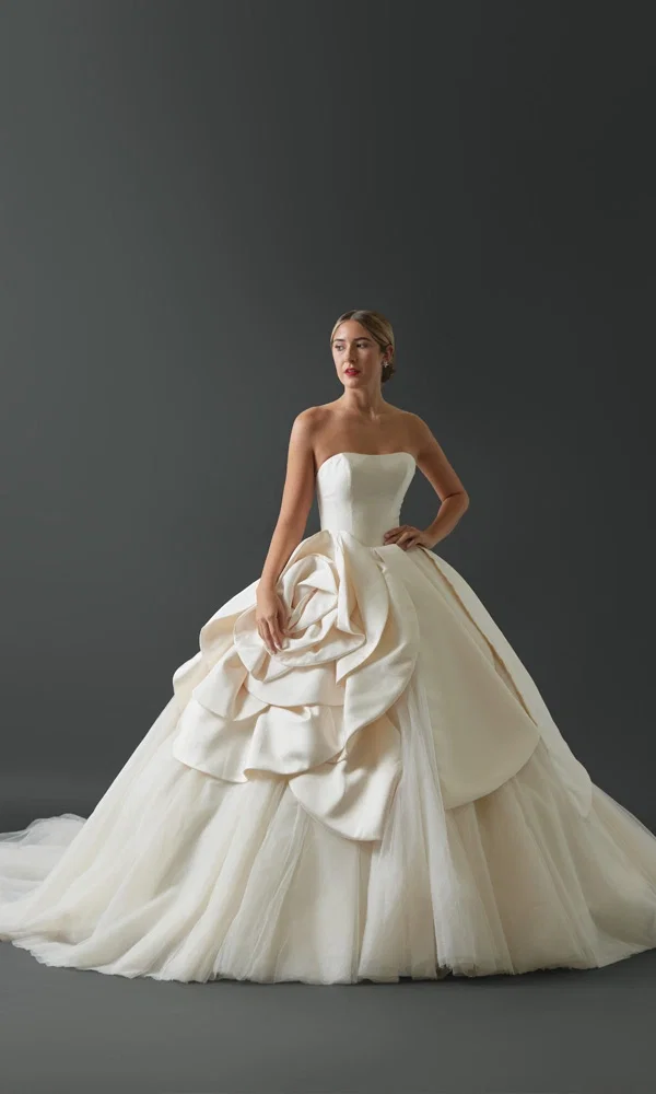 Großartiges Brautkleid mit voluminöser Silhouette und floraler Drapierung, das klassische Eleganz und moderne Extravaganz kombiniert.