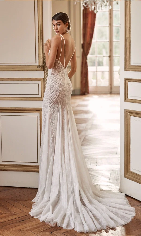 Traumhaftes Brautkleid mit transparenten Spitzendetails und langer Schleppe, das eine feminine Eleganz in einem luxuriösen Raum unterstreicht.