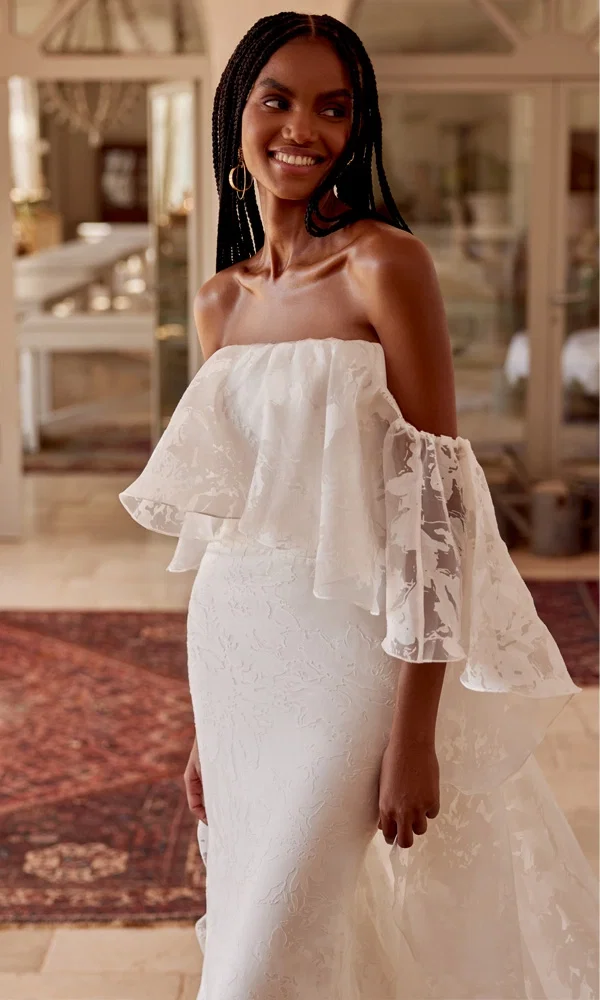 Braut in einem modernen, geblümten Spitzenkleid mit verspielten Glockenärmeln – ungezwungen und elegant zugleich.