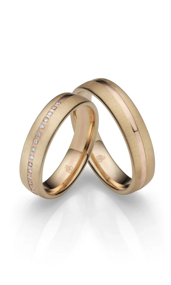 Ein Paar moderner Trauringe in Gold mit mattem Design: der Damenring geschmückt mit Diamanten, der Herrenring veredelt durch einen Roségold-Akzent.