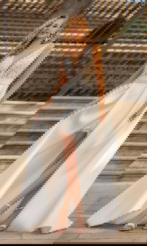 Verspieltes Brautkleid im Lingerie-Stil mit auffälligen Ohrringen und langem Satin-Overskirt – fotografiert vor klassischer Kulisse.