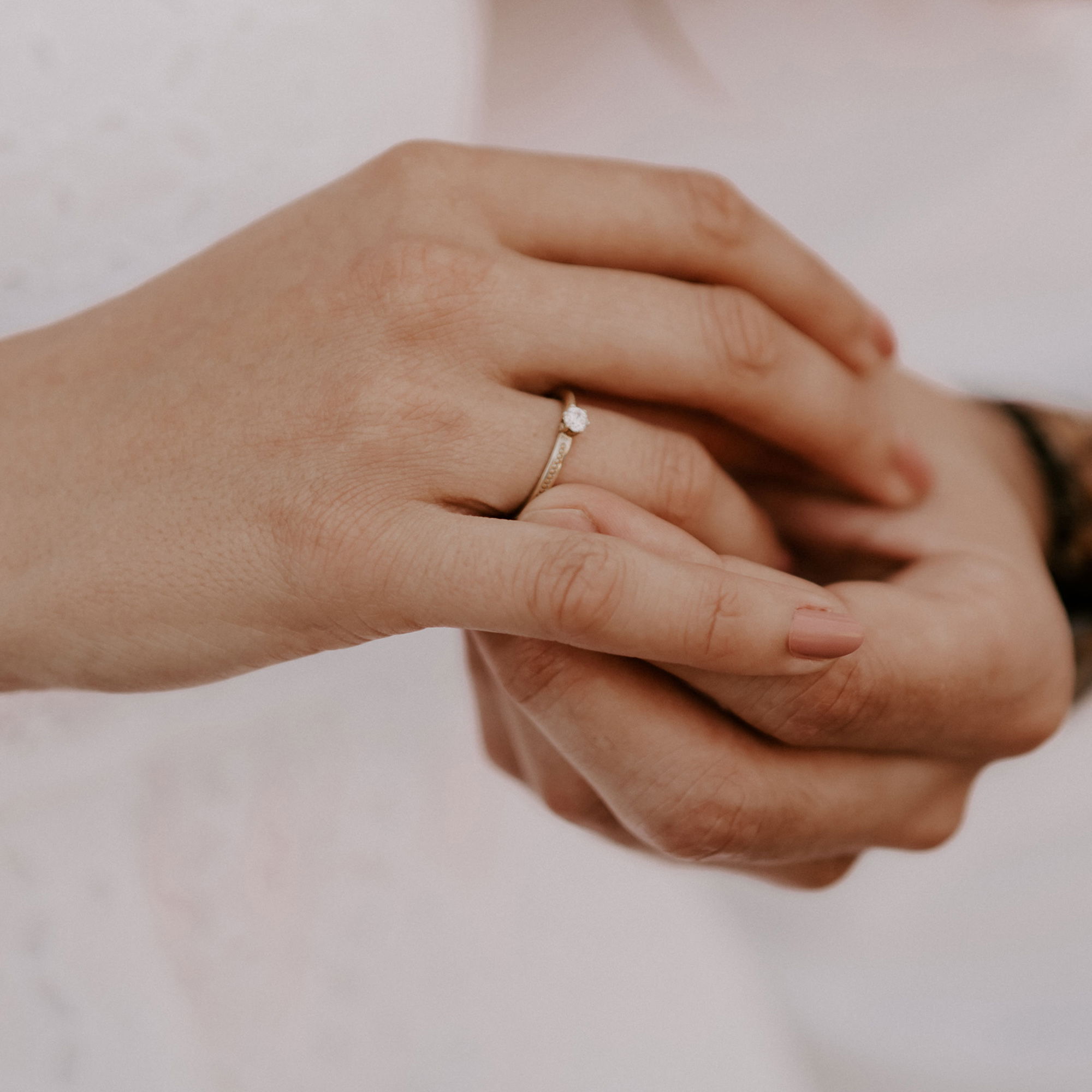 Goldener Verlobungsring mit Diamant in der Hand einer Frau, liebevoll gestützt von einer weiteren Hand, Symbol für Verlobung und Liebe.