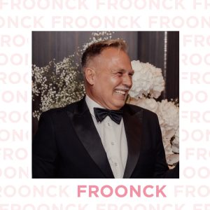 Porträt von Froonck in schwarzem Smoking, umgeben von stilvollen Blumenarrangements und mit einem strahlenden Lächeln.